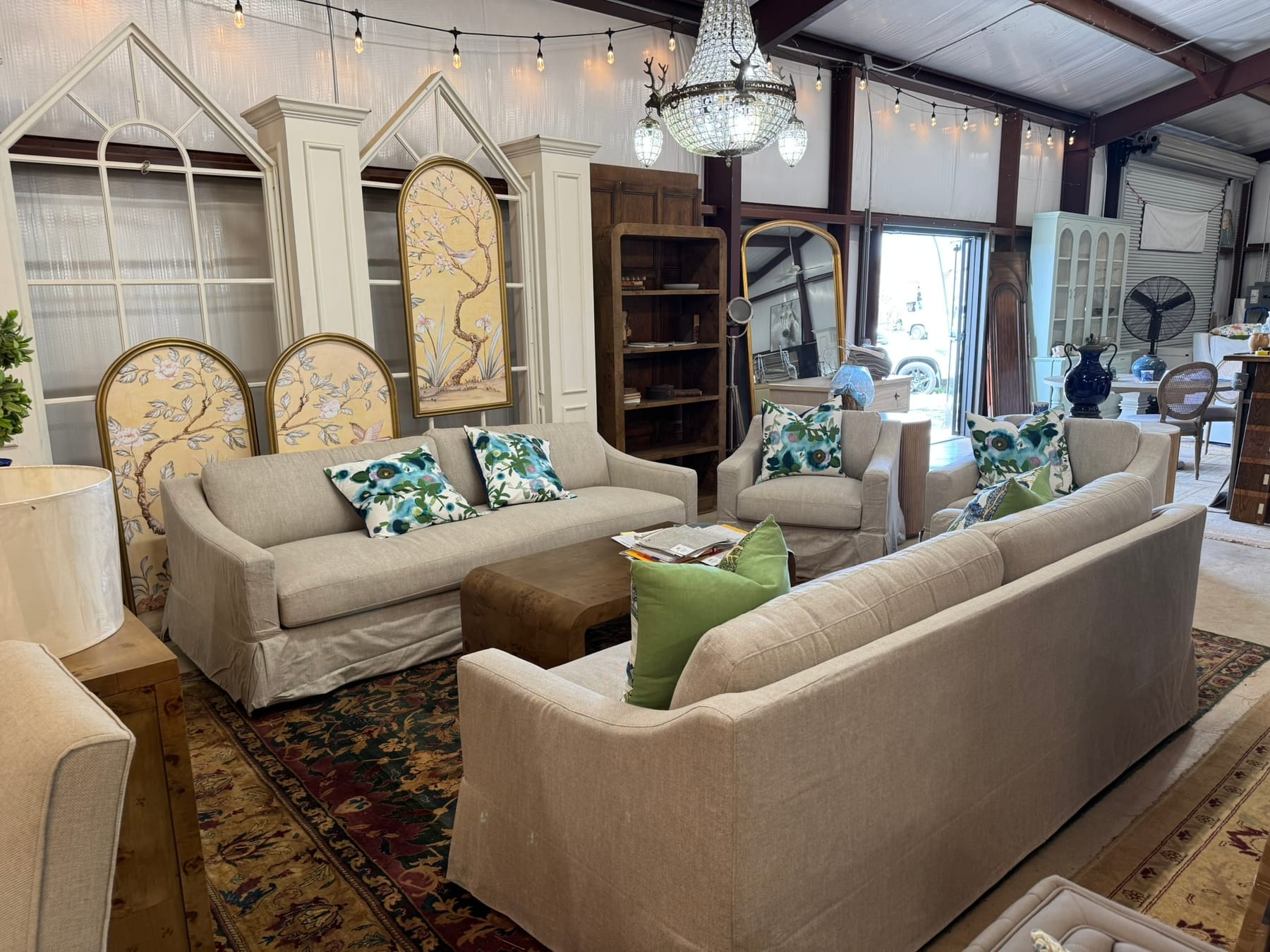 Inside the Adams booth at Round Top — linen slipcovered sofas and armchairs around a burl coffee table under a crystal chandelier, with gilt-framed chinoiserie panels behind