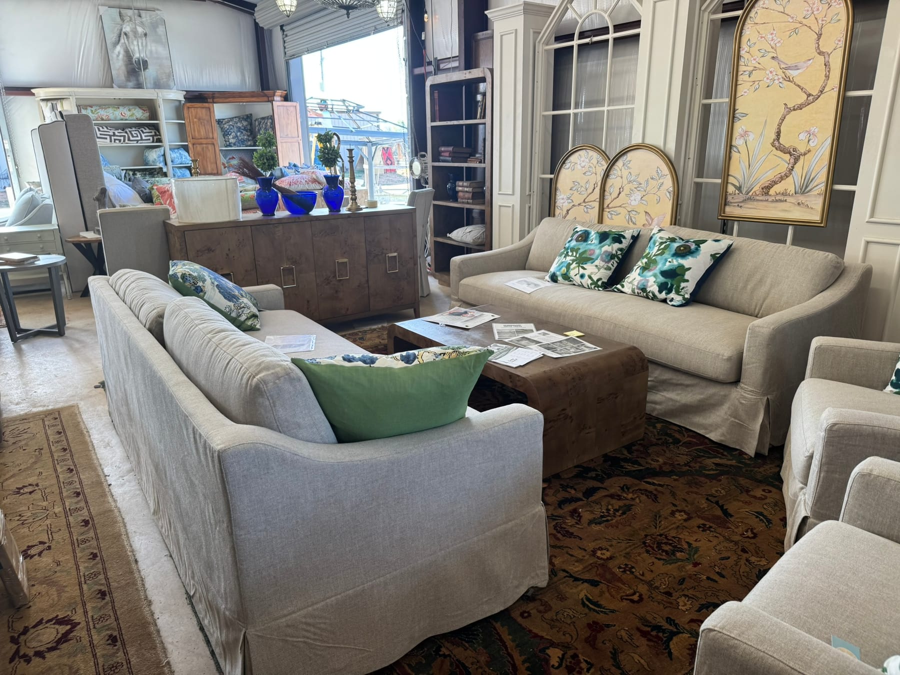 A pair of slipcovered sofas facing each other over a burl waterfall coffee table, with a burl sideboard, cobalt glass, and arched chinoiserie panels behind