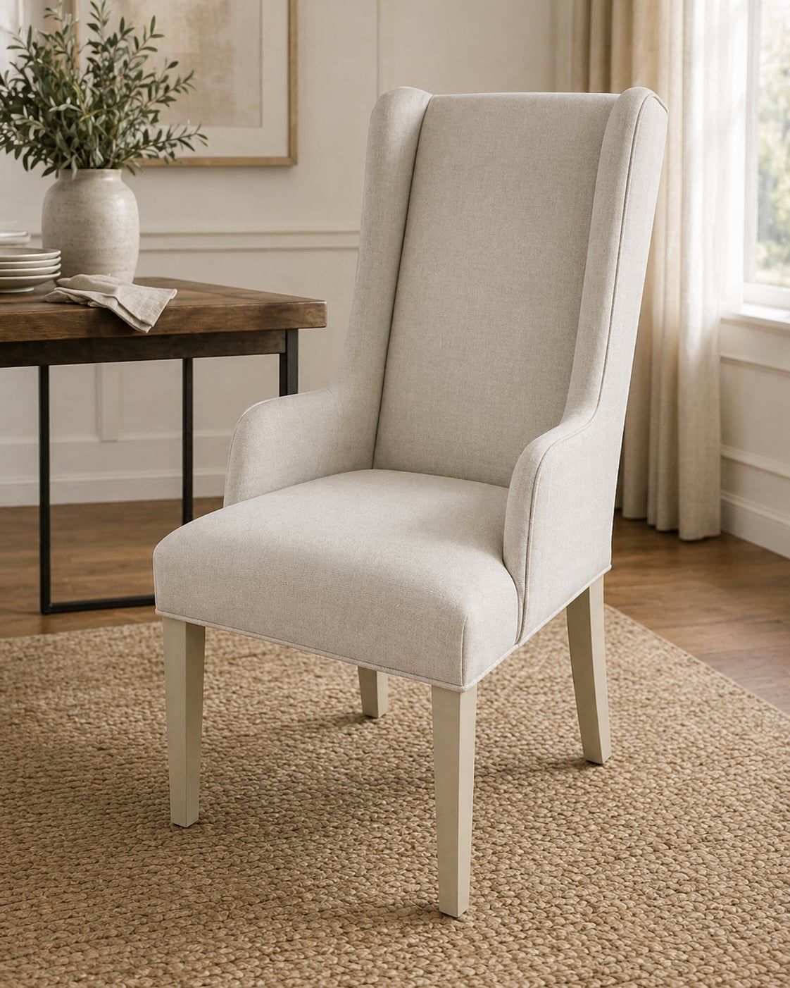 Cream wingback host chair beside a wood dining table with stoneware vase